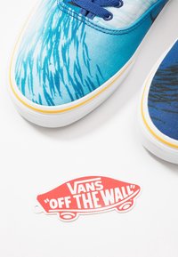 Sneaker di tela blu con design a motivo d'acqua, suola in gomma bianca, rifiniture gialle e lacci blu. Include il tag del logo Vans rosso.