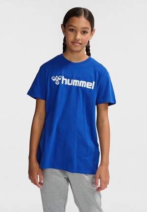 Blå bomulds t-shirt med rund halsudskæring og korte ærmer, med en hvid 'hummel' logo trykt foran. Båret sammen med grå bukser.