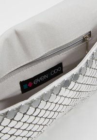 Silberne Mesh-Clutch mit sechseckigem Muster; innen mit einem cremefarbenen Stofffutter und einer Reißverschlusstasche ausgestattet. Das Etikett trägt die Aufschrift "even&ODD."
