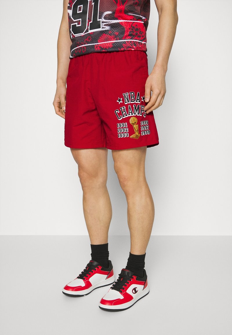 Röda basketshorts med texten "NBA CHAMP" och mästerskapsår tryckt i vitt och gult. Bars med svarta strumpor och röda sneakers.