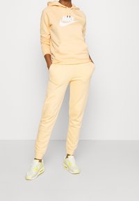 Jasnożółta bluza Nike z dużym białym logo, w połączeniu z dopasowanymi dresami i białymi sneakersami z żółtymi akcentami.