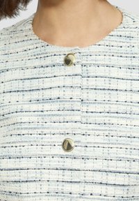 White and blue tweed jacket featuring a textured weave, round gold buttons, and a cropped collarless design.