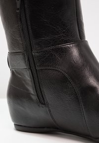 Bottine en cuir noir avec une finition texturée, fermeture éclair sur le côté et talon courbé. Présente des détails de couture et un design élégant.