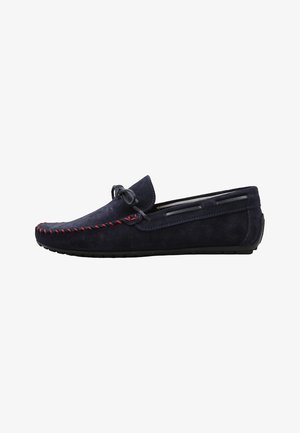 Mocassin pour homme en daim bleu marine avec détails de surpiqûres rouges, nœud en lacets sur le dessus et semelle en caoutchouc noir, vue de côté sur fond blanc.