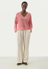Stripet rød og hvid strikket V-hals sweater parret med letvægts, cremefarvede linned bukser med vide ben og brune sko.