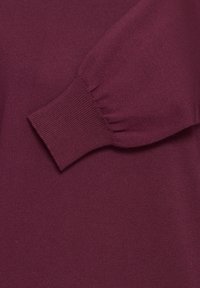 Poignet de manche longue avec poignet élastiqué sur un vêtement tricoté de couleur prune montré en gros plan.