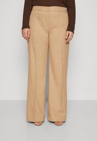 Beige wide-leg trousers with a textured finish, featuring a front button closure and crease lines, styled over pale beige sandals.