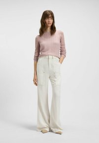 Maglione lavorato a maglia di un rosa chiaro con maniche lunghe, abbinato a pantaloni bianchi a gamba larga con ampie tasche frontali e cuciture sottili.