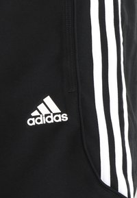 Mustat urheiluhousut, jotka on valmistettu teksturoidusta kankaasta, joissa on kolme valkoista raitaa sivussa ja valkoinen Adidas-logot oikealla sääressä.