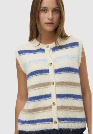 Vrouw draagt een mouwloze, zachte, gebreide spencer met blauw, beige en witte horizontale strepen en houten knopen aan de voorkant.