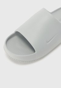 Light gray slide sandal with a wide strap and textured footbed. Features a subtle Nike logo and ridged sole for grip. Smooth, rubber material.