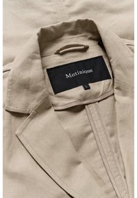 Beige jacket featuring a textured fabric, notched collar, and interior label with the brand "Matinique." Includes a concealed zip closure.
