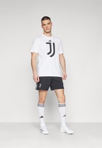 Hvid atletisk skjorte med sort Juventus-logo, sorte shorts med hvide accenter og knælange hvide sokker med sorte striber.