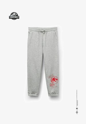 Pantalons de survêtement en coton gris avec une taille élastique et un cordon de serrage. Présente des graphiques de dinosaures rouges et du texte sur la jambe gauche. Chevilles resserrées.