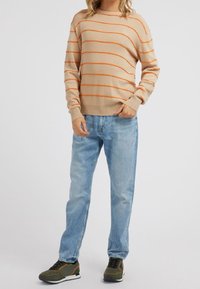 Beige trui met oranje horizontale strepen, ronde hals, geribde manchetten, gecombineerd met lichtblauwe jeans en groene sneakers.