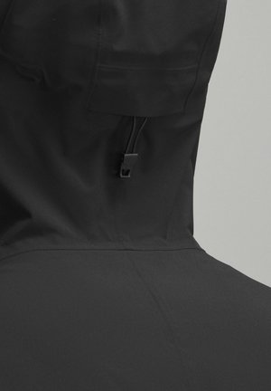 Veste imperméable noire avec un col haut et un cordon de serrage ajustable, texture lisse et design minimaliste sans motifs supplémentaires.