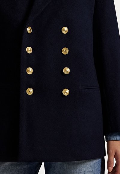 Marineblauer, doppelt gefütterter Wollmantel mit sechs goldenen Knöpfen und einer Seitentasche. Strukturierte Form mit softem Gefühl und minimalistischem Stil.