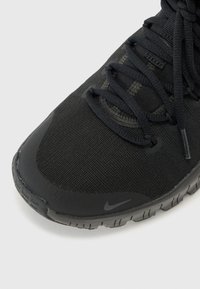 Scarpa sportiva nera con tomaia in rete testurizzata, lacci piatti e suola in gomma flessibile. Presenta una punta liscia e dettagli del logo discreti.