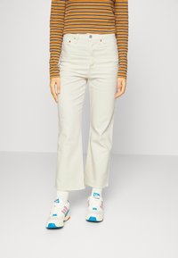 Vaqueros blancos de pierna ancha, confeccionados en denim, presentan una cinturilla alta y costuras sutiles. Combinados con una camiseta de rayas de manga larga y zapatillas coloridas.