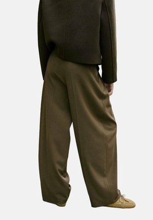 Pantalones de pierna ancha en tela verde oliva, con una textura suave y un diseño plisado, combinados con una chaqueta corta oscura y calzado claro.