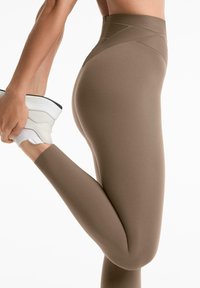 Hoge taille, bruine legging van een gladde, rekbare stof; voorzien van diagonale textuuraccenten op de tailleband en een strakke enkel.