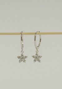Boucles d'oreilles en argent en forme de créole avec des pendentifs en forme d'étoile ornés de pierres transparentes et scintillantes, présentant une finition lisse et polie.