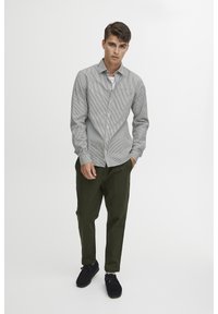 Grijs en wit gestreepte button-up shirt met lange mouwen, gecombineerd met donkergroene broek en zwarte schoenen. Eenvoudig ontwerp zonder zichtbare patronen.
