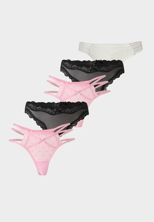 Jeune femme debout pieds nus portant un soutien-gorge en dentelle blanche et une culotte assortie sur un fond uni clair.