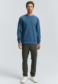 Hanorac albastru din material moale, cu guler rotund și manșete ribbed. Asortat cu pantaloni întunecați texturati și adidași albi.