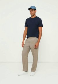 Μπλουζάκι με κοντά μανίκια σε ναυτικό μπλε, μπεζ παντελόνια και λευκά αθλητικά παπούτσια. Ένα ανοιχτό μπλε καπέλο ολοκληρώνει τη στολή. Απλό, άνετη εφαρμογή, χωρίς ορατά λογότυπα.