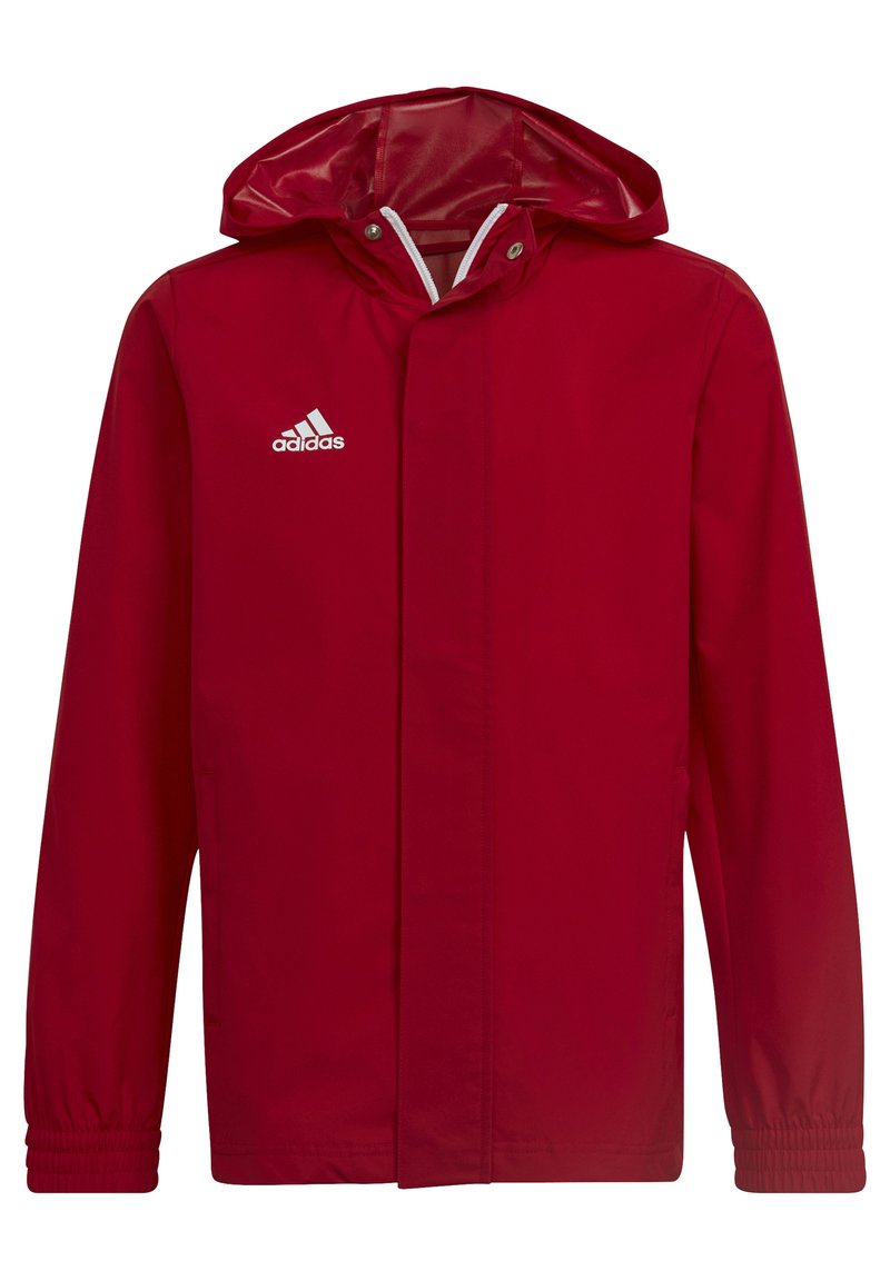Veste imperméable rouge avec capuche, poignets élastiques, bandes blanches et logo brodé blanc sur la poitrine gauche. Texture douce.