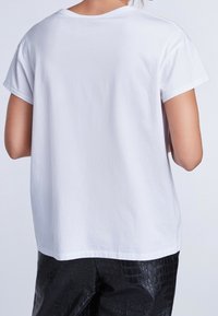 Camiseta blanca de algodón con un corte relajado, cuello redondo y mangas cortas, combinada con pantalones de cuero sintético negro de imitación de cocodrilo.