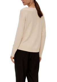 Hellbeige Pullover mit lässigem Schnitt, geripptem Saum und Bündchen, langen Ärmeln, kombiniert mit lockeren schwarzen Hosen.