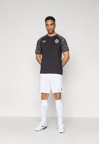 Sort sports t-shirt med mønstrede skuldre, blå accenter, hvide shorts, hvide sokker og sorte fodboldstøvler. Enkel design og atletisk pasform.