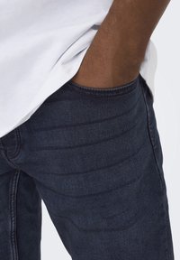 Jeans de mezclilla azul oscuro con bolsillos visibles, presentan una textura suave y un sutil detalle de desgaste en la tela.