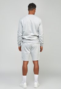 Completo in cotone grigio composto da felpa e pantaloncini, con scollo rotondo e polsini a coste, abbinato a calzini bianchi e scarpe da ginnastica, visto da dietro.