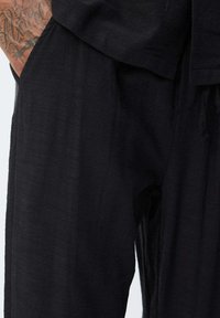 Pantalons en lin noir avec un tissu texturé, présentant une coupe ample et des jambes larges. Aucun fermoir ni motif visible.