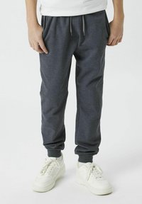Graue Sweatpants mit elastischen Bündchen und Bund, aus weichem Stoff. Kombiniert mit weißen Sneakers, die ein strukturiertes Obermaterial und eine dicke Sohle haben.