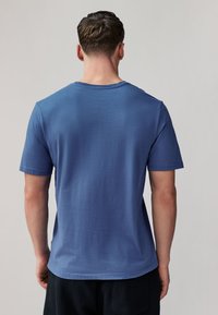 Rövid ujjú, kerek nyakú póló kék anyagból. Egyenletes textúrájú, szabályos szabással, minimalista dizájnnal és egyenes alsó szegéllyel.