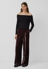 Schwarzer Off-Shoulder-Pullover mit langen Ärmeln, kombiniert mit hochtaillierten, dunkelburgunderfarbigen, weit geschnittenen Samthosen. Strukturiert, maßgeschneiderte Passform.