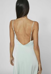 Bakvy av en ljus mintgrön klänning med tunna axelband, djup V-formad rygg och en mjuk, flödande tygtextur.