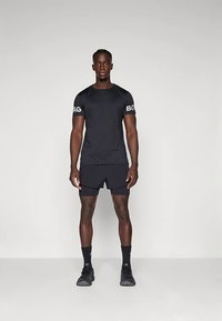 Juoda sportinė marškinėliai ir šortai, su apvalia kaklo linija ir logotipu ant rankovės. Tekstūruota medžiaga, lygi paviršius ir prigludęs dizainas.