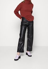 Svetr s rolákem v rustikální barvě, černé kalhoty z umělé kůže širokého střihu a světle fialové mokasíny s robustní černou podrážkou. Viditelné detaily texturované látky.