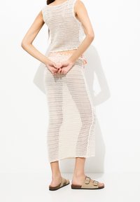 Top in maglia all'uncinetto beige e gonna lunga con spacchi laterali, abbinati a sandali marroni con due fibbie.