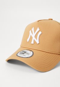 Brun baseball caps med en hvit brodert logo, buet skjerm, teksturert stoff og en justerbar bakre stropp merket "New Era."