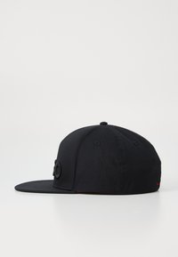 Casquette de baseball noire à visière plate, en coton. Elle présente un logo circulaire à l'avant, avec des coutures à l'arrière.