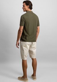 Donkergroene polo met korte mouwen, in een iets getailleerde pasvorm; gecombineerd met lichtbeige shorts en beige instapschoenen.