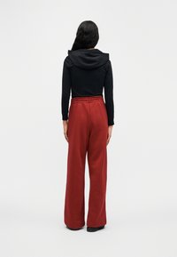 Μαύρο μπλουζάκι με μακριά μανίκια και κουκούλα, συνδυασμένο με κόκκινο φαρδύ παντελόνι φόρμας με ελαστική μέση και φαρδιά πόδια.