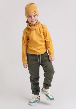 Żółta koszula z długim rękawem, dopasowana czapka typu beanie, zielone spodnie z kieszeniami oraz białe trampki z turkusowymi i beżowymi akcentami.