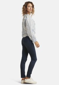Light blue, textured blouse with floral embroidery, long sleeves gathered at the cuffs. Paired with dark skinny jeans and white sneakers.